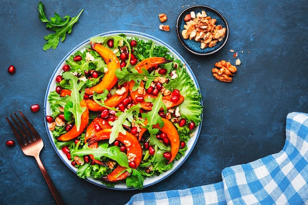 Ensalada de calabaza para comer sano con calabaza dulce horneada, lechuga, rúcula, semillas de granada y nueces Comida reconfortante Fondo azul Vista superior