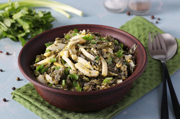 Ensalada con calamares de algas y cebollas verdes en tazón marrón sobre fondo azul claro Primer plano