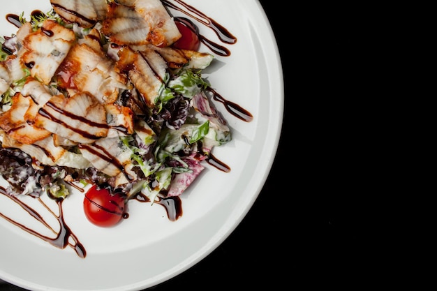 Ensalada de calamares, lechuga, col, tomates cherry y salsa. Ensalada con rodajas de calamar, sobre un plato blanco, sobre fondo negro. primer plano de la foto, enfoque suave. Foto para libro de recetas, menú de restaurante