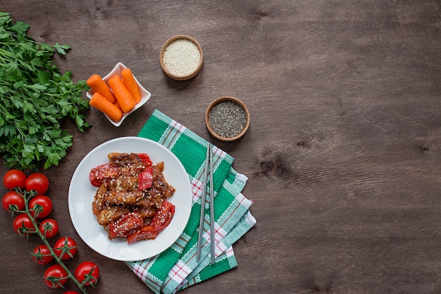 Ensalada caliente de berenjenas y tomate al estilo coreano con semillas de sésamo y hierbas Comida asiática. Plato vegetariano. Madera. .