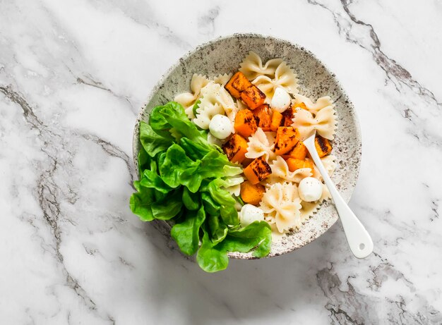 Ensalada caliente de mozzarella de pasta de mariposa de calabaza al horno en una vista superior de fondo claro