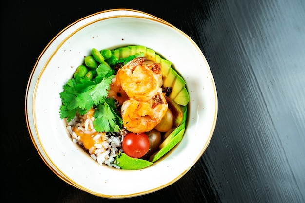 Ensalada con camarones fritos, arroz, aguacate, judías verdes y tomates cherry en un recipiente amarillo sobre un fondo oscuro.