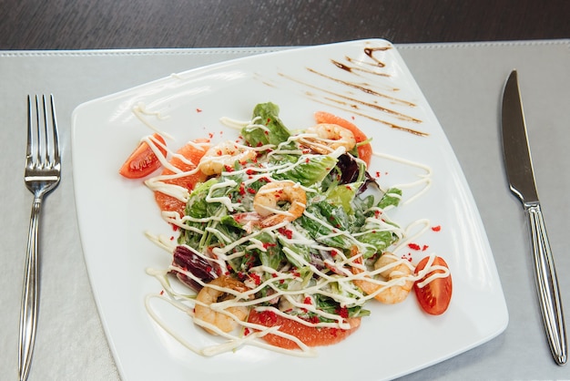 Ensalada con camarones, rodajas de salmón, tomates, verduras en un plato sobre la mesa