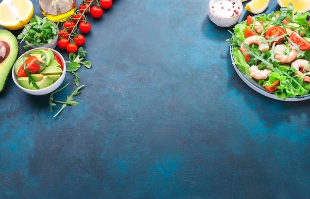 Ensalada de camarones con tomates, lechuga, rúcula, aguacate, pepino y aderezo de limón en la mesa azul. Concepto de comida limpia y saludable para comer Vista superior