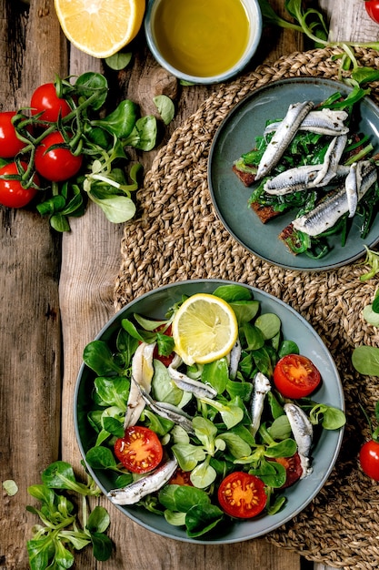 Ensalada de campo verde con filete de anchoas en escabeche o sardinas y tomates cherry, servido en cuenco azul con limón y aceite de oliva