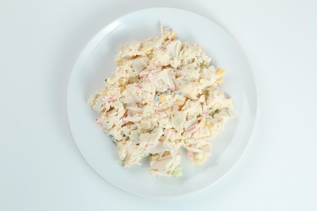 Ensalada de cangrejo con arroz en primer plano de la placa blanca con espacio de copia. Ensalada tradicional rusa con palitos de cangrejo aislado en blanco