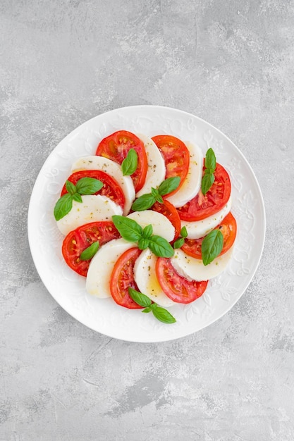 Foto ensalada caprese clásica con queso mozzarella, tomates y albahaca en una placa blanca.