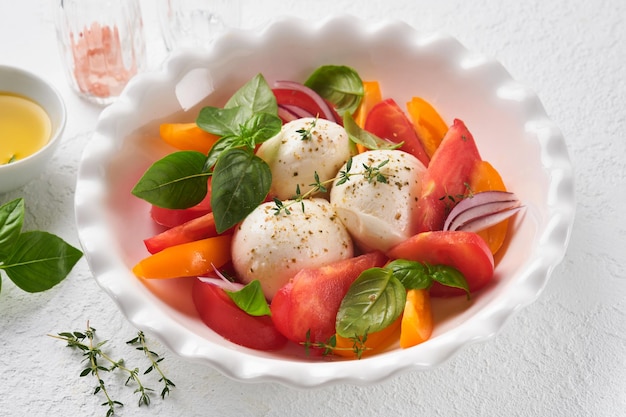 Ensalada caprese Ensalada caprese italiana con rodajas de tomate queso mozzarella albahaca aceite de oliva en un plato blanco sobre fondo blanco Deliciosa comida italiana Vista superior Estilo rústico