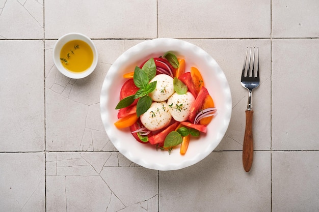 Ensalada caprese Ensalada caprese italiana con rodajas de tomate queso mozzarella albahaca aceite de oliva en un plato blanco sobre fondo blanco Deliciosa comida italiana Vista superior Estilo rústico