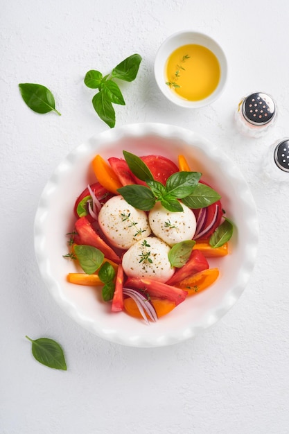 Ensalada caprese Ensalada caprese italiana con rodajas de tomate queso mozzarella albahaca aceite de oliva en un plato blanco sobre fondo blanco Deliciosa comida italiana Vista superior Estilo rústico