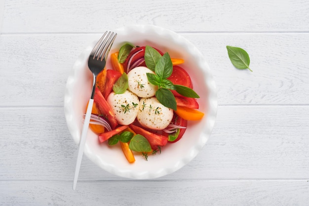 Ensalada caprese Ensalada caprese italiana con rodajas de tomate queso mozzarella albahaca aceite de oliva en un plato blanco sobre fondo blanco Deliciosa comida italiana Vista superior Estilo rústico