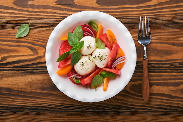 Ensalada caprese Ensalada caprese italiana con rodajas de tomate queso mozzarella albahaca aceite de oliva en plato blanco sobre fondo de madera vieja Deliciosa comida italiana Vista superior Estilo rústico