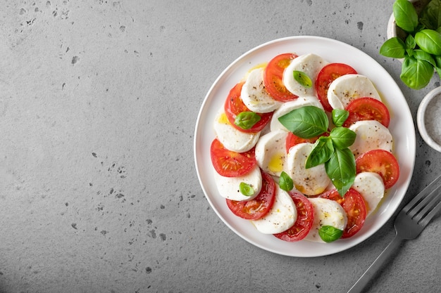 Ensalada caprese italiana con rodajas de tomate mozzarella albahaca aceite de oliva sobre un fondo gris vista superior ...