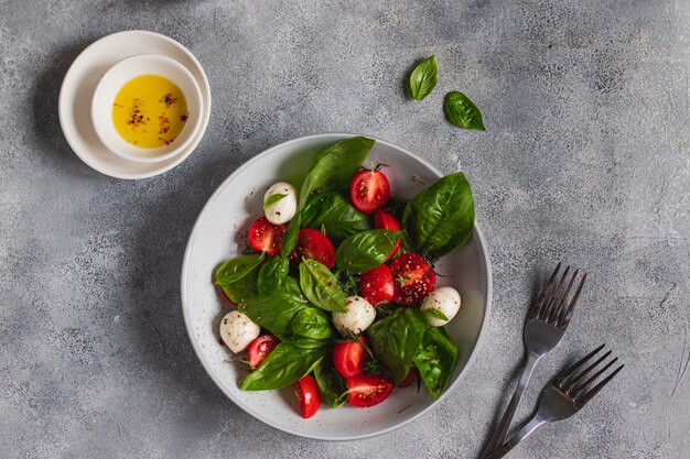 Ensalada caprese italiana con rodajas de tomate, mozzarella, albahaca, aceite de oliva sobre un fondo gris