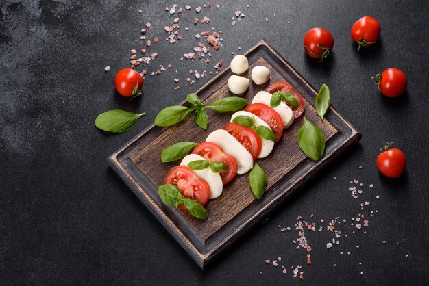 Ensalada caprese italiana con rodajas de tomate, queso mozzarella, albahaca, aceite de oliva. Servido en plato vintage negro sobre un fondo de hormigón oscuro