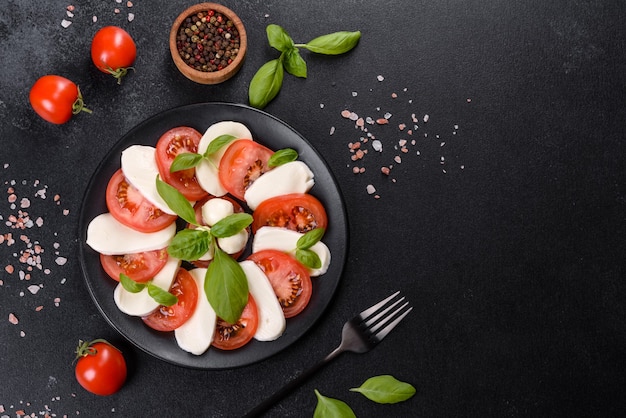 Ensalada caprese italiana con rodajas de tomate, queso mozzarella, albahaca, aceite de oliva. Servido en plato vintage negro sobre un fondo de hormigón oscuro