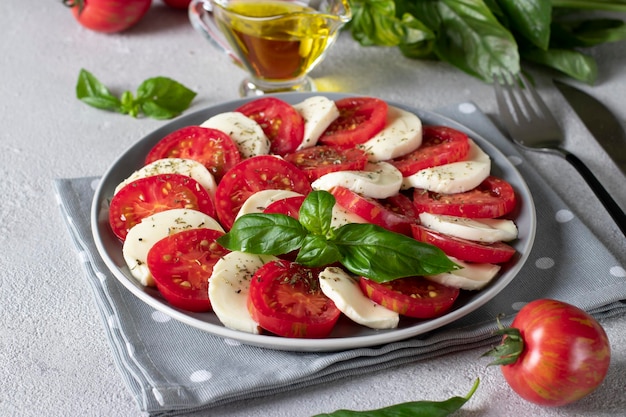 Ensalada caprese italiana con rodajas de tomate queso mozzarella albahaca y aceite de oliva sobre fondo gris claro