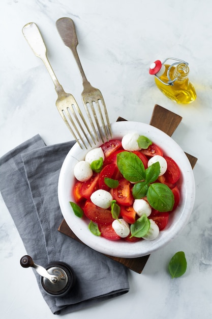 Ensalada caprese italiana tradicional con tomates, queso maozzarella y albahaca sobre una superficie de mármol claro en un plato de cerámica blanca vieja. Enfoque selectivo Vista superior. Copie el espacio.