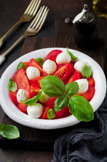Ensalada caprese italiana tradicional con tomates, queso mozzarella y albahaca sobre fondo oscuro en blanco plato de cerámica antigua.