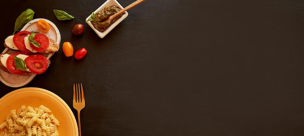 Ensalada caprese de pasta fusilli italiana con aperitivo de mozzarella de tomate y albahaca con pesto sobre fondo rústico negro Pancarta extra ancha Vista superior comida Cena italiana Espacio de copia