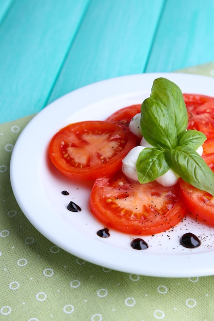 Ensalada Caprese con queso mozarella, tomates y albahaca en un plato sobre fondo de mesa de madera