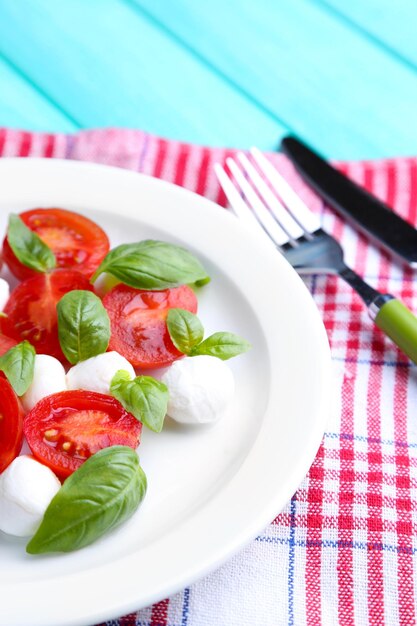 Ensalada Caprese con queso mozarella, tomates y albahaca en un plato sobre fondo de mesa de madera