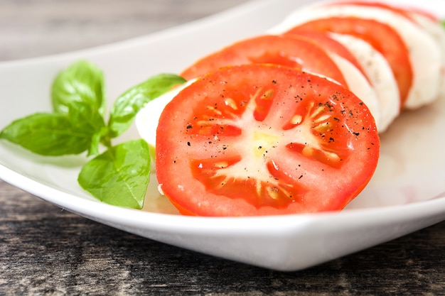 Ensalada Caprese con queso mozzarella y albahaca sobre madera rústica