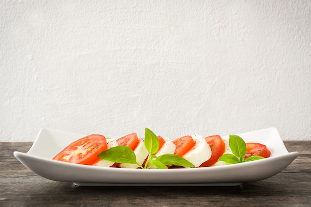 Ensalada Caprese con queso mozzarella y albahaca sobre madera rústica