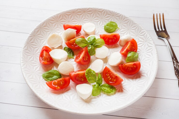 Ensalada Caprese de tomates, queso mozzarella y albahaca en un plato blanco. Cocina italiana.