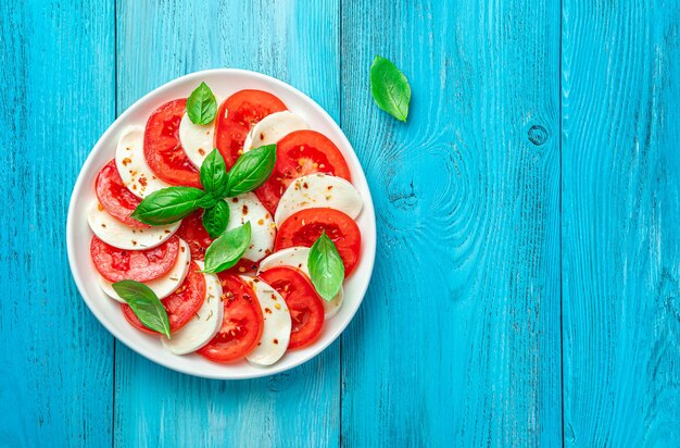 Ensalada caprese tradicional con pamidors, mazzarella, albahaca y aceite de oliva sobre un fondo azul claro. Cocina italiana. Vista superior, el espacio para copiar.