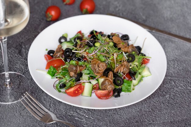 Ensalada de caracol, aceituna, tomate cherie, pepino, verduras sobre fondo oscuro.