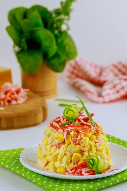 Ensalada de carne de cangrejo con maíz dulce, queso y huevos decorada con chips de maíz y pepino. Foto vertical.