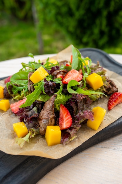 Ensalada con carne, fresas, mango sobre una tabla de madera negra Resort de lujo