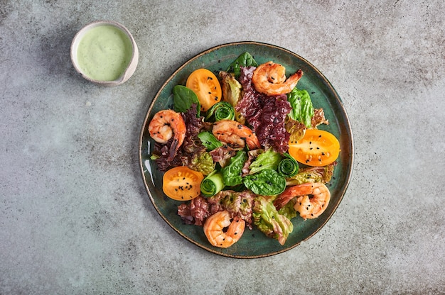 Ensalada casera con camarones fritos, tomates amarillos, rúcula, espinacas, lechuga y salsa en un plato de cerámica, vista superior