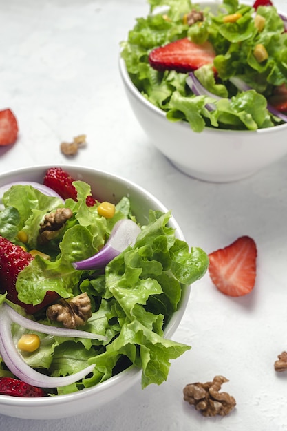 Ensalada casera con lechuga, fresas, cebolla morada, maíz; aceite de oliva y nueces en un bol. Concepto de comida vegana