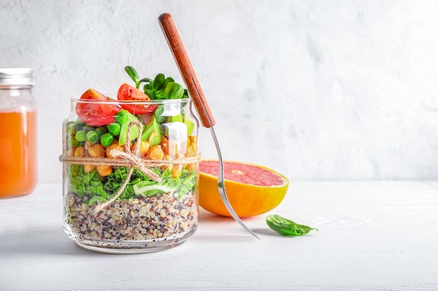 Ensalada casera saludable en frasco de vidrio con quinua, verduras y hierbas om fondo blanco. Concepto de comida vegana.