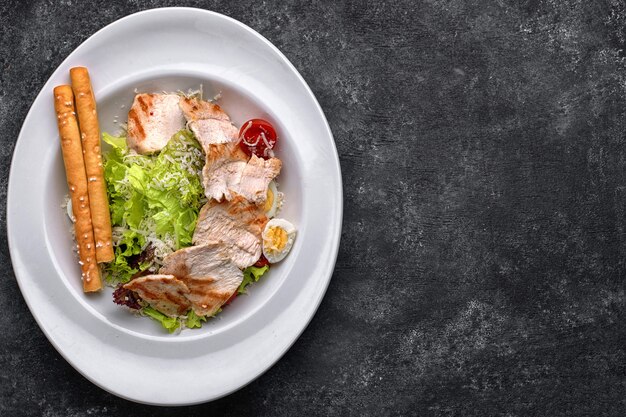 Ensalada César con carne de pollo, lechuga, tomate, queso y huevos, sobre una placa blanca.