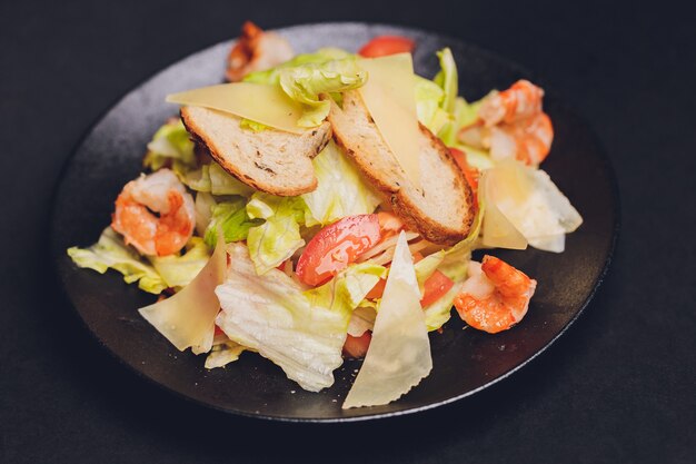 Ensalada César clásica con pechuga de pollo a la plancha y medio huevo en plato de cerámica blanca. Servido con los ingredientes arriba sobre fondo antiguo de madera azul oscuro. Vista superior, espacio.