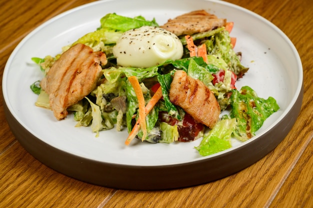 Ensalada César con crutones, huevos de codorniz, tomates cherry y pollo asado en mesa de madera. Deliciosa ensalada con pollo, nueces, huevo y verduras.