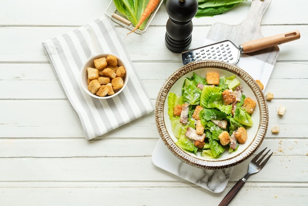 Ensalada César fresca en placa en la mesa blanca de madera. Comida sana, vista superior