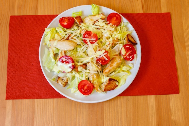 Ensalada César fresca y saludable con pecho de pollo, tomates de cereza, lechuga, salsa de queso parmesano y croutones en una mesa de madera.