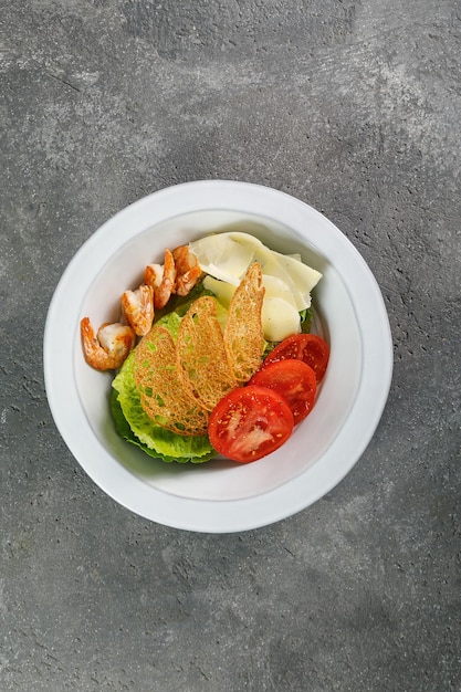 Ensalada César con gambas en plato blanco sobre fondo de hormigón gris