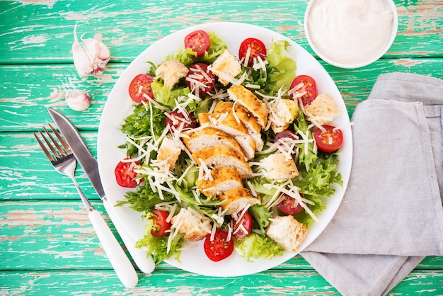 Ensalada César con pechuga de pollo sobre un fondo rústico, tomates, parmesano, ensalada verde y picatostes, enfoque selectivo, vista superior