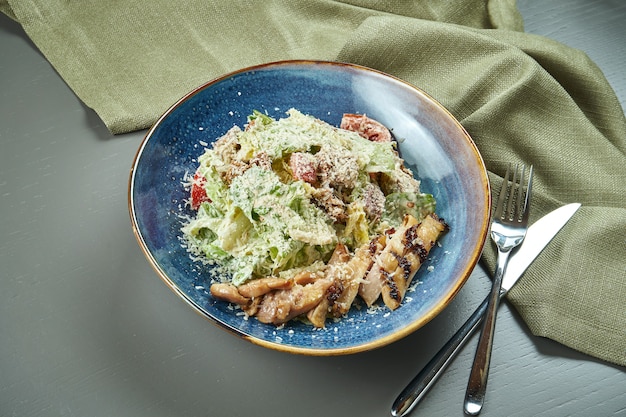 Ensalada César con picatostes, parmesano, pollo, huevo en un tazón azul sobre mesa de madera. Restaurante de servicio. De cerca