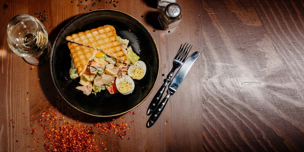 Ensalada César en plato negro sobre mesa de madera.