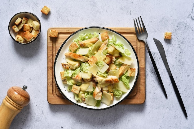 Ensalada César en un plato sobre una tabla de madera sobre un fondo de hormigón, vista superior.