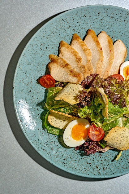 ensalada César con pollo y huevo en un plato sobre un fondo gris