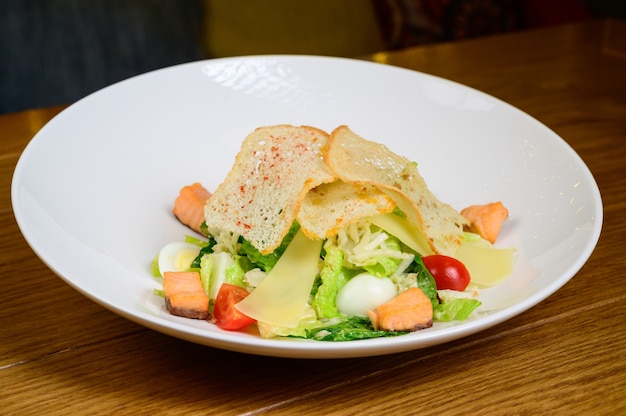 Foto ensalada césar con salmón en plato blanco sobre fondo de madera ensalada césar con salmón, vista superior