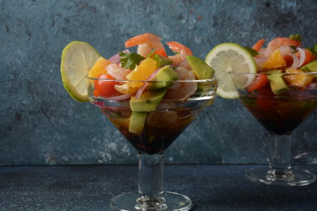 Ensalada de ceviche con camarones, naranjas y aguacate en recipiente de vidrio sobre un fondo oscuro o gris. Comida latinoamericana. Delicioso ceviche de camarones recién hecho. Camarones marinados en lima y naranja.