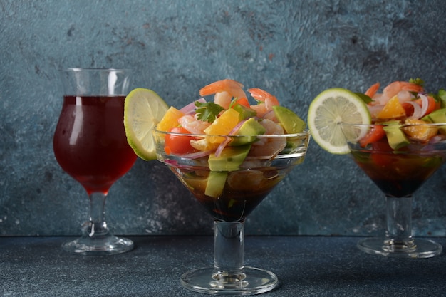 Ensalada de ceviche con camarones, naranjas y aguacate en recipiente de vidrio sobre un fondo oscuro o gris. Comida latinoamericana. Delicioso ceviche de camarones recién hecho. Camarones marinados en lima y naranja.